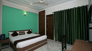 Una habitación de hotel con cama, escritorio, silla, ventilador de techo y cortina verde.