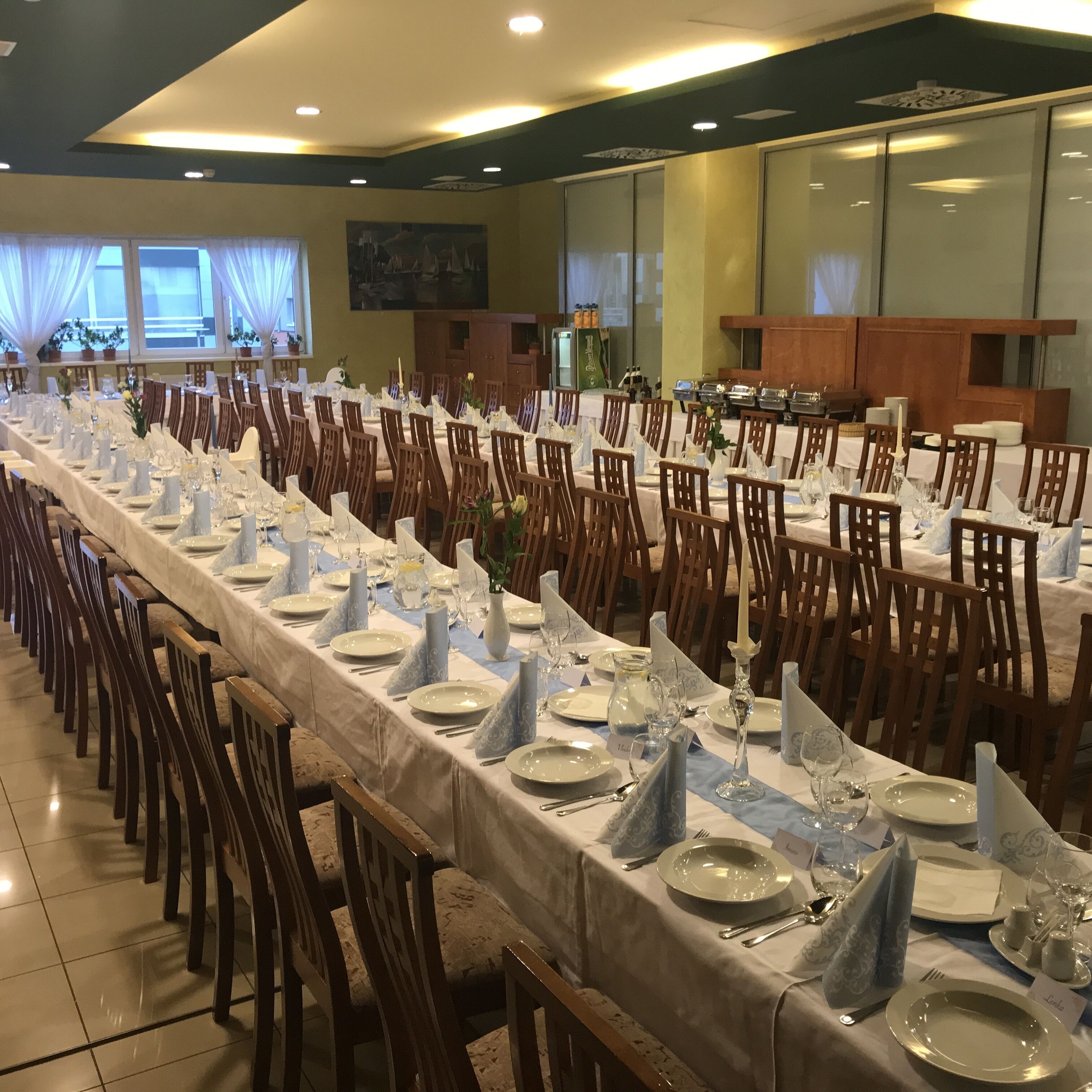 Una larga mesa de banquete con manteles blancos, servilletas azules y cubertería.