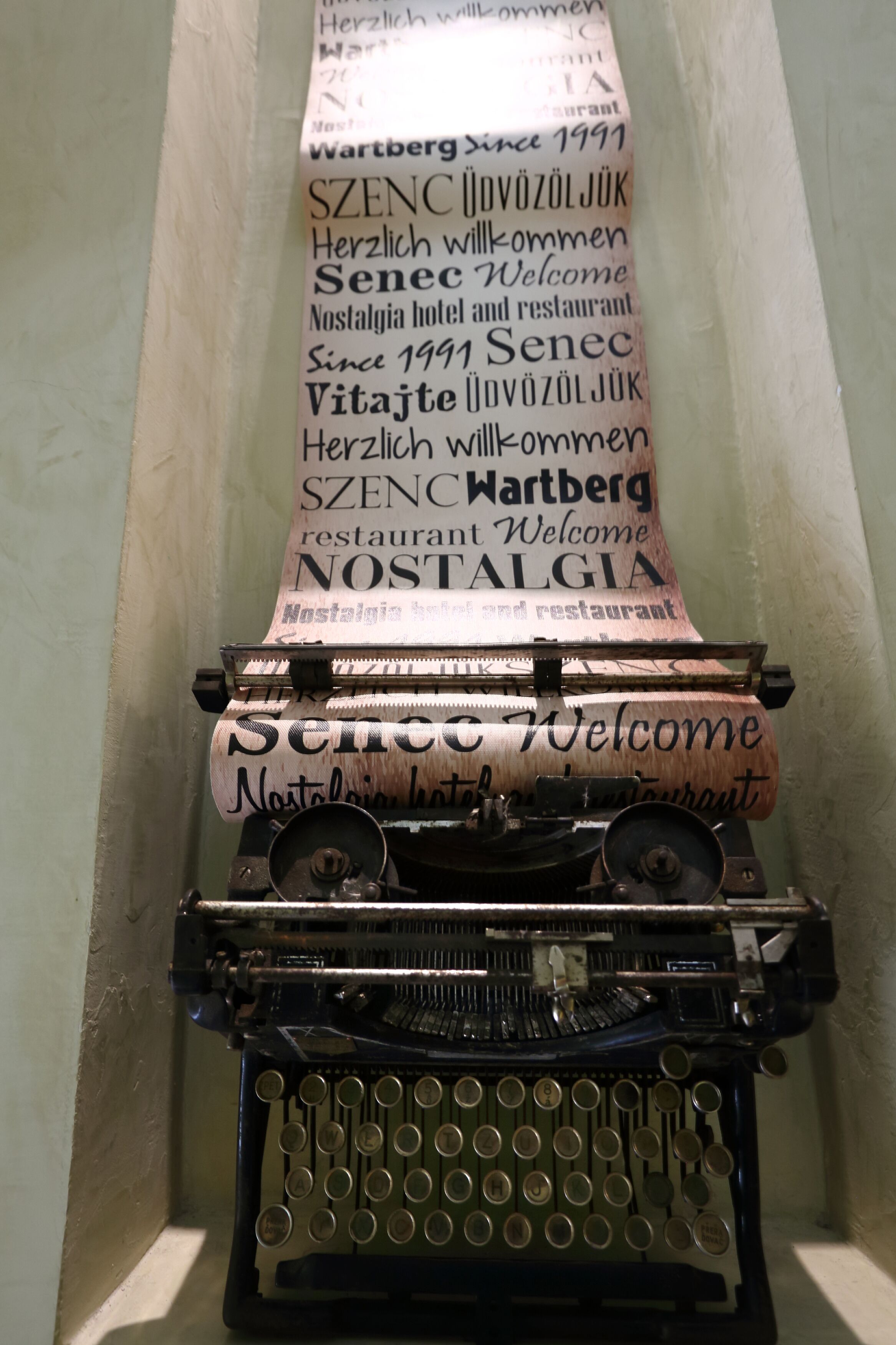 A vintage typewriter with a rolled-up sheet of paper displaying 'SENEC Welcome Nostalgia hotel and restaurant'.