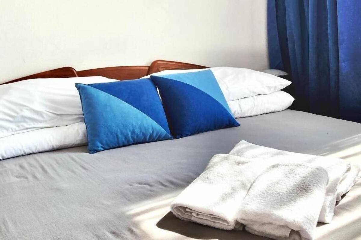 A neatly made bed with white and blue pillows, a grey bedspread, and a folded white towel on the side.