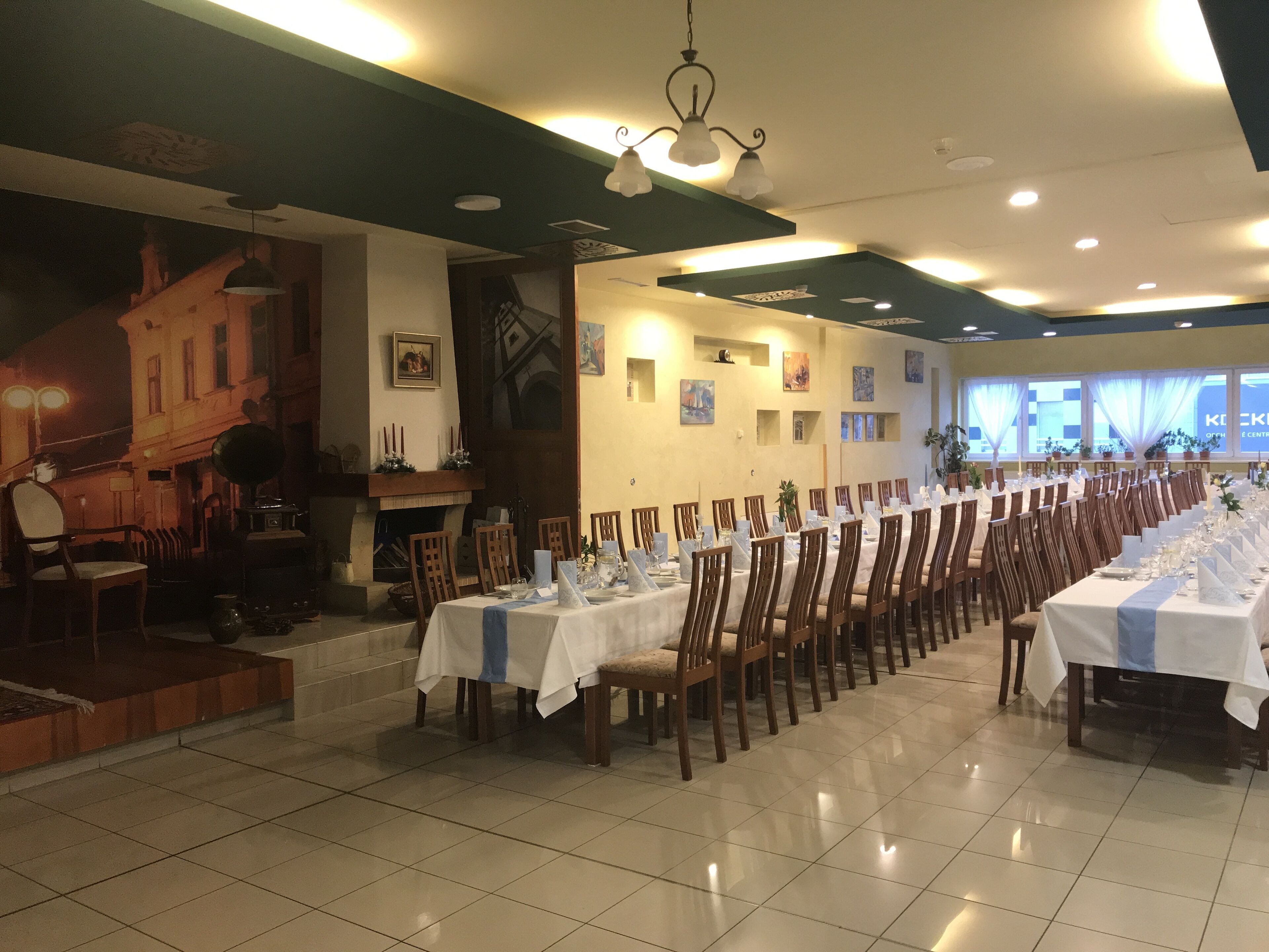 Uma longa mesa de jantar com cadeiras, um palco com um piano e um mural na parede.