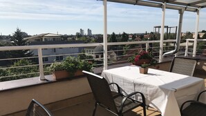 Un balcon avec une table et des chaises, des plantes en pot et une vue sur le paysage urbain.