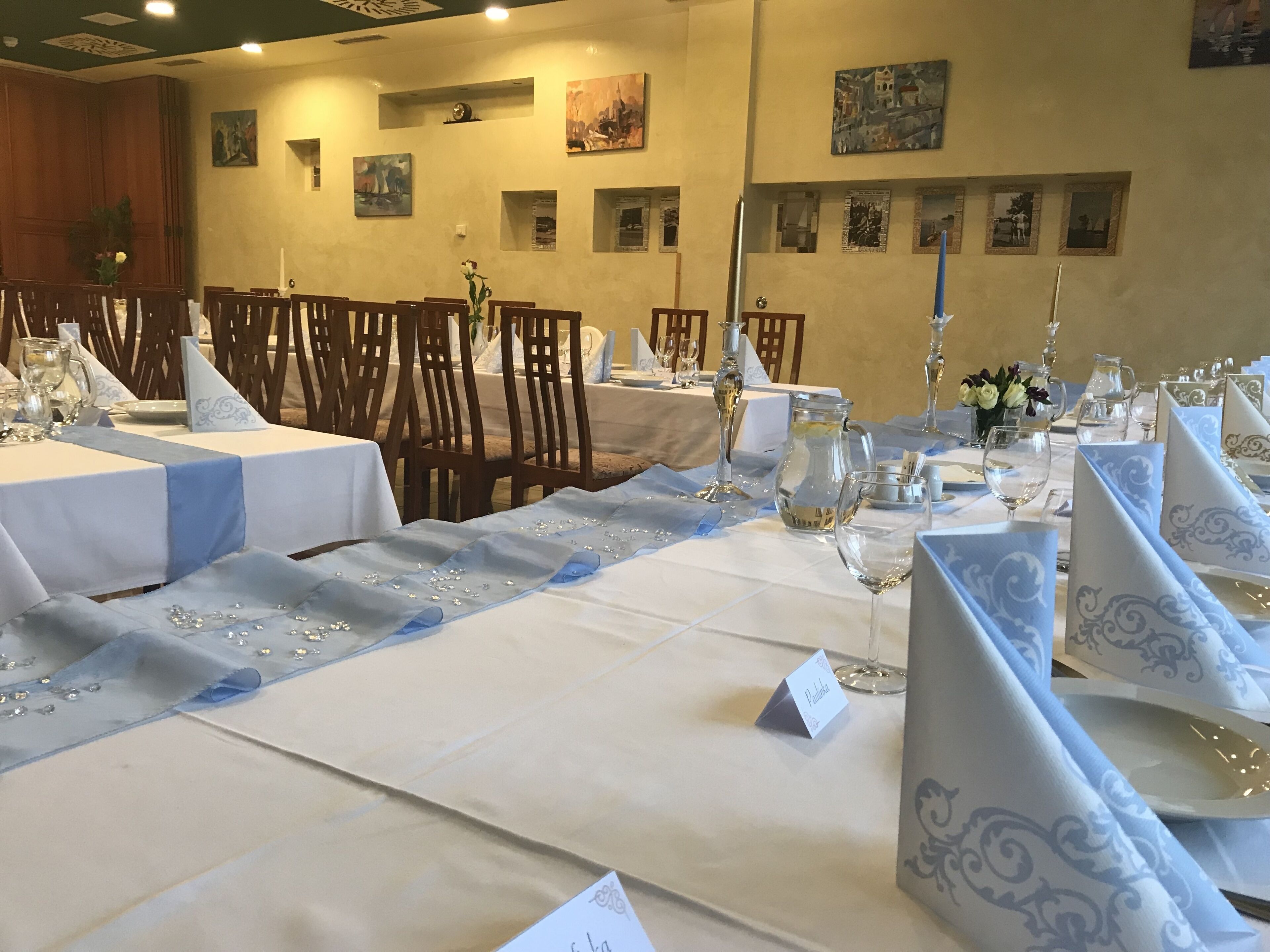 Un salón de banquetes con mesas dispuestas para un evento formal, con manteles blancos, servilletas azules y cristalería.