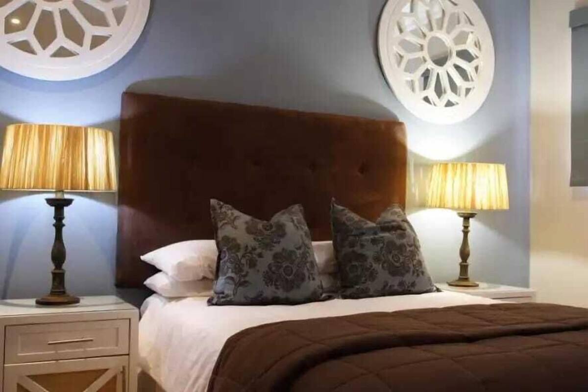 Ein Schlafzimmer mit einem braunen, gepolsterten Kopfteil, zwei Nachttischen mit Lampen und dekorativen Wandleuchten.