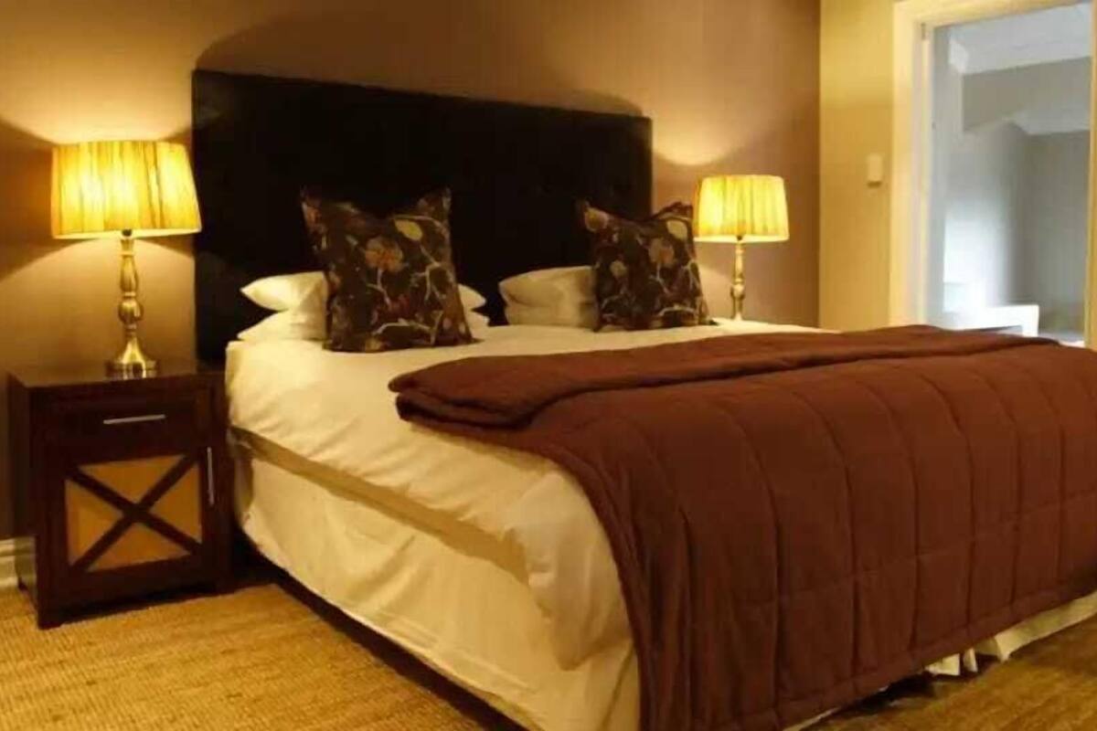 Ein ordentlich bezogenes Bett mit einer braunen Decke, zwei Kissen und zwei Nachttischlampen.
