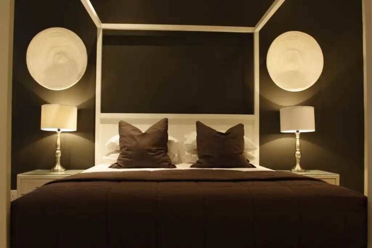 Ein Schlafzimmer mit einem Himmelbett, zwei Nachttischlampen und einem dunkel gefärbten Kopfteil.