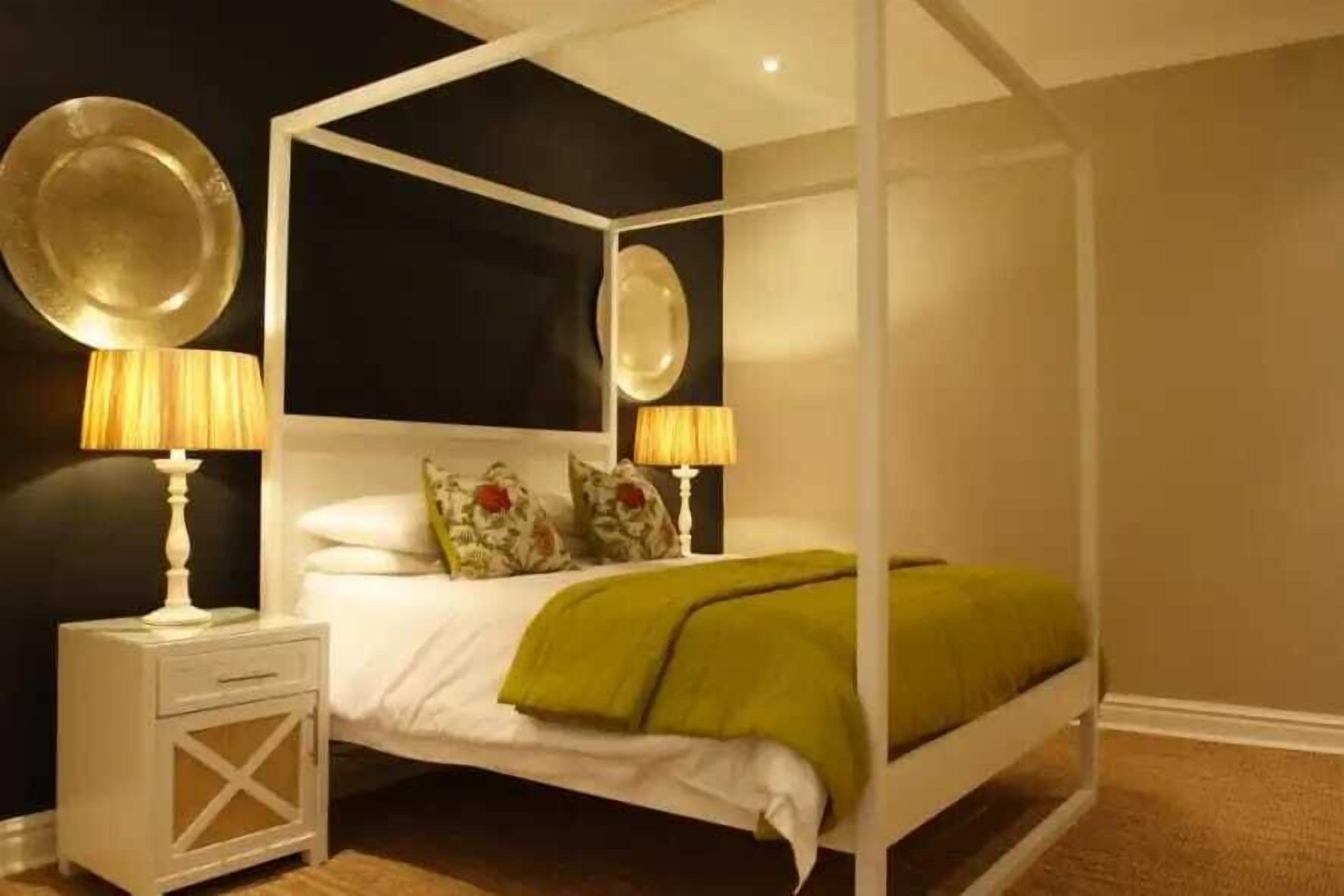 A four-poster bed with a white frame, two bedside lamps, and a green throw blanket.