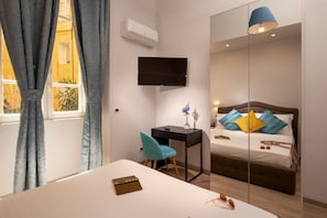 A bedroom with a bed, a desk, a chair, a TV, and a window with curtains. - The Shell Rome Suite (Rome)
