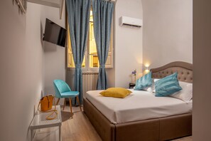 A bedroom with a bed, a chair, a table, and a TV. - The Shell Rome Suite (Rome)