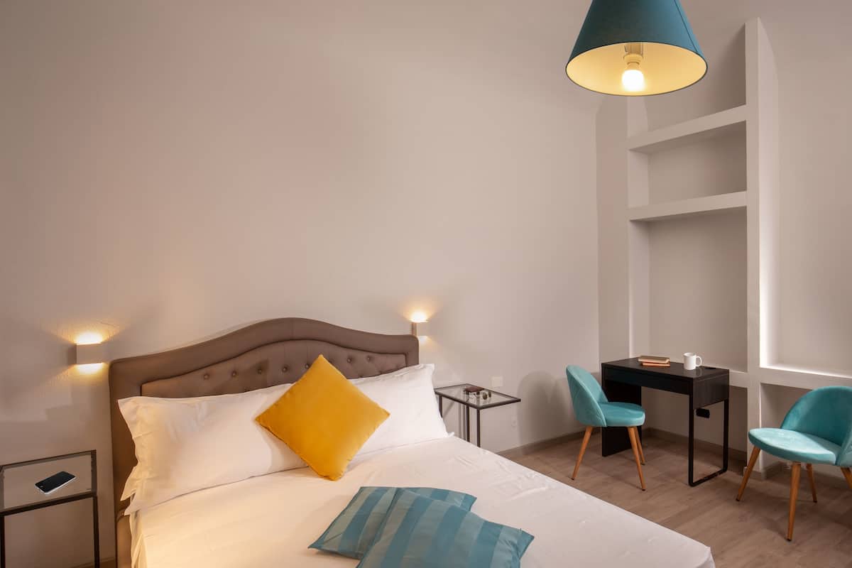 A neatly arranged bedroom with a bed, bedside tables, a desk, and chairs.
