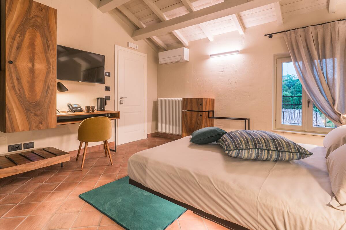 A bedroom with a bed, a desk, a chair, a TV, and a window with curtains.