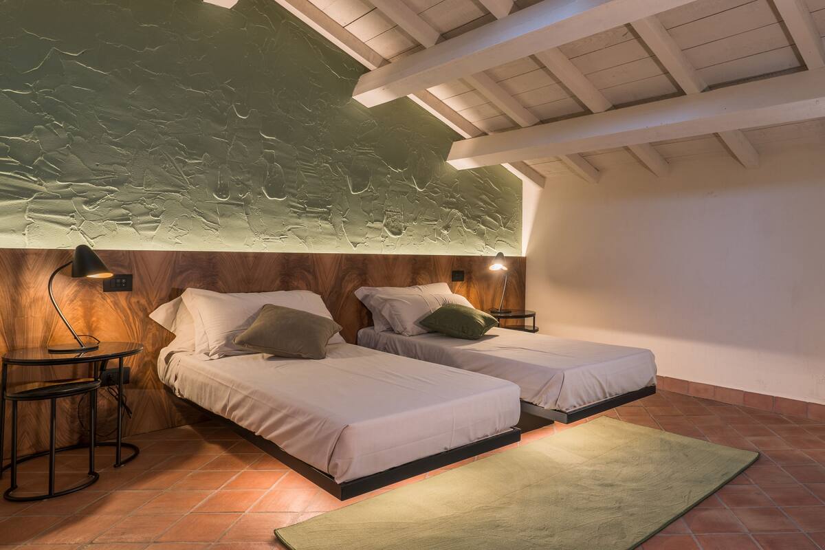 A bedroom with two beds, a wooden headboard, a green wall, and a tiled floor.