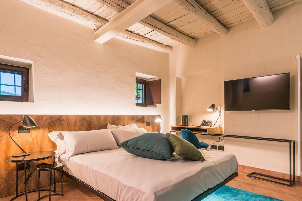 A bedroom with a bed, bedside tables, a desk, a chair, a TV, and a window.