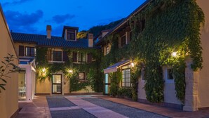 A courtyard with a tiled floor, a building covered in ivy, and a lit entrance. - Cà Toresele Relais Osteria Garden (Verona)