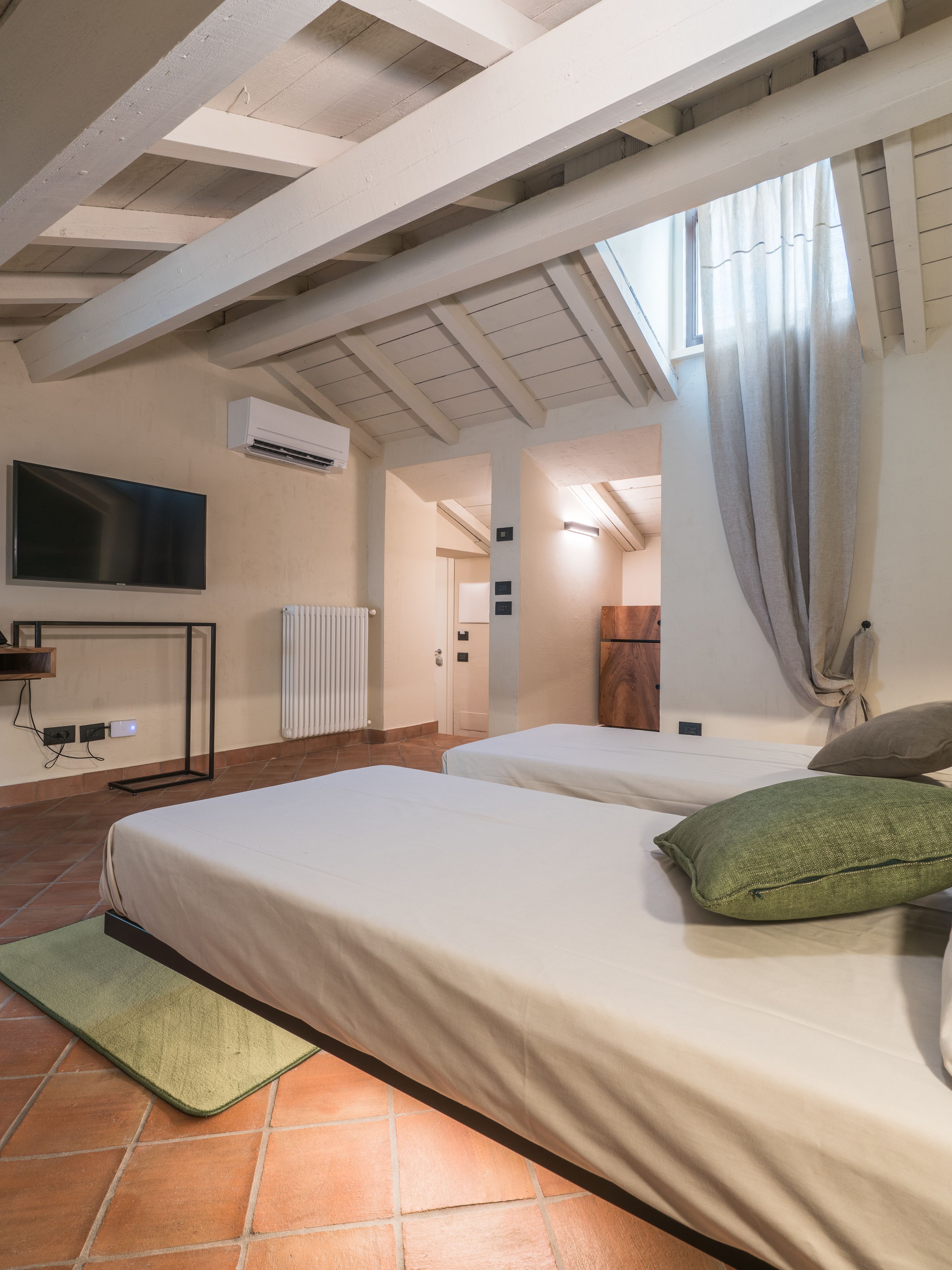 A bedroom with two beds, a TV, and a window with curtains.