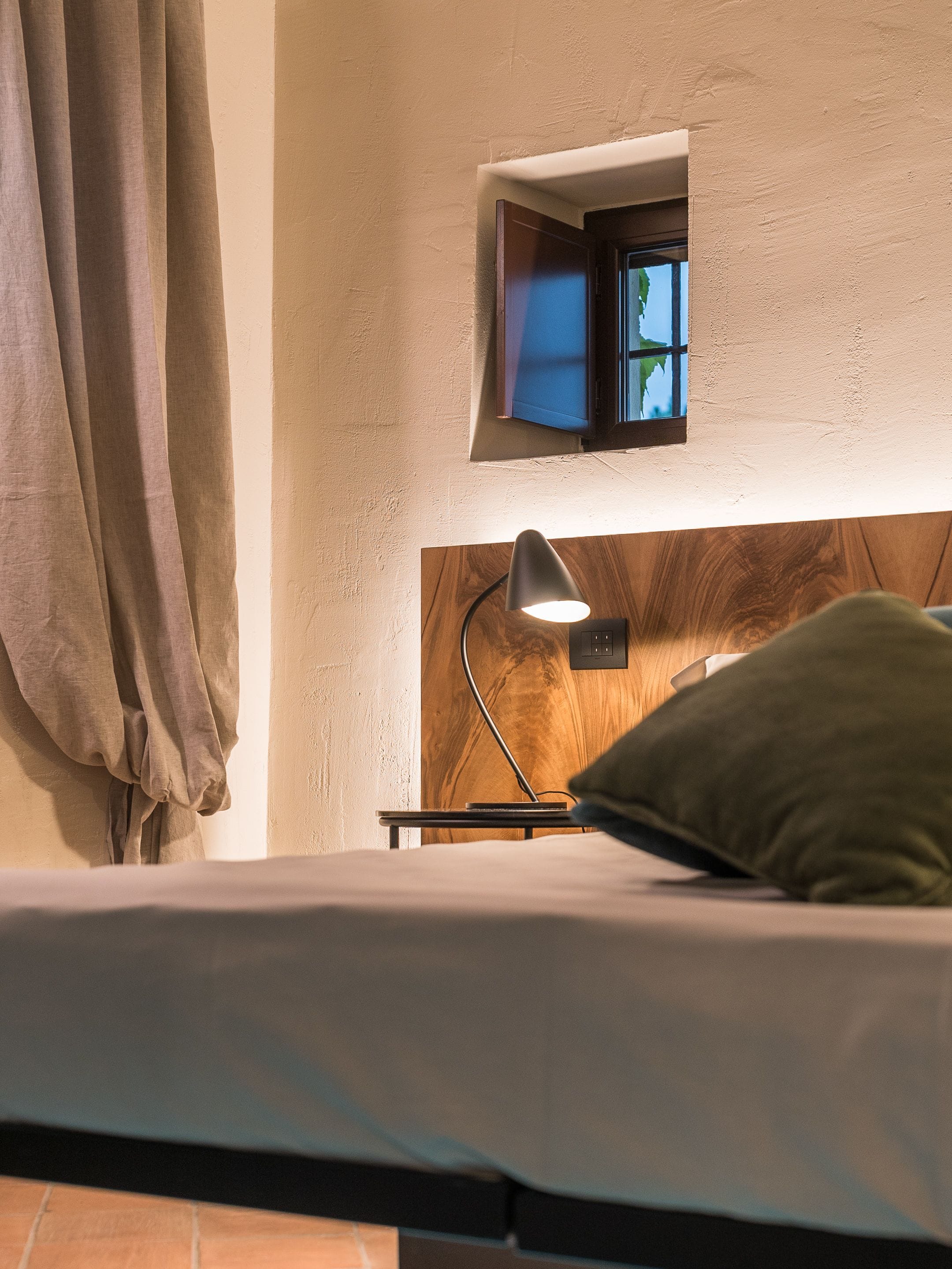 A bedroom with a bed, a nightstand, a lamp, a window, and a curtain.