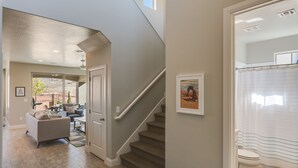 Amplia sala de estar con una escalera que sube a un segundo piso, un baño moderno con cortina de ducha y vistas al exterior.