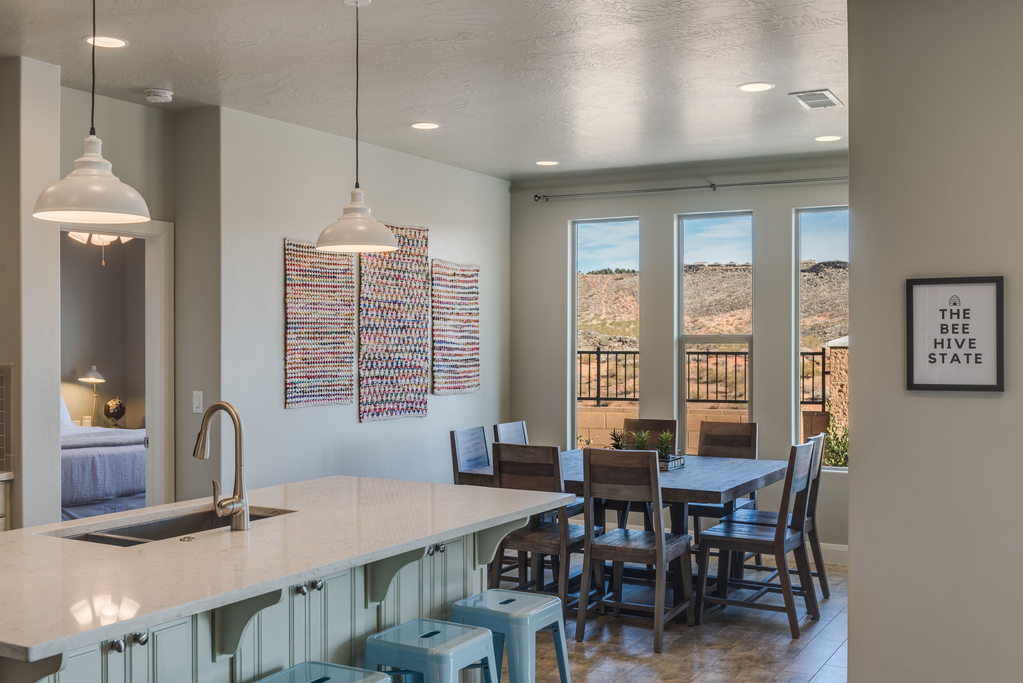 A kitchen with a large island, pendant lights, and a view of the desert through large windows.