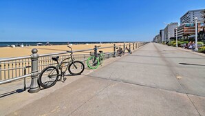 Un paseo marítimo con bicicletas estacionadas a lo largo de la barandilla, cielo despejado y edificios al fondo.