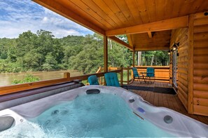 Una terraza de madera con un jacuzzi, sillas y vistas a un río y un bosque.