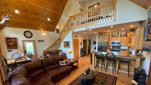 A spacious living room with a large brown leather sofa, a coffee table, and a staircase leading to an upper level.