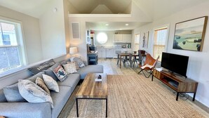 A modern living room with a sofa, coffee table, and TV. There is a kitchen in the background with a dining area. - Beach Nut Bungalow:  Two bedroom home in Pamlico Point (Ocracoke)