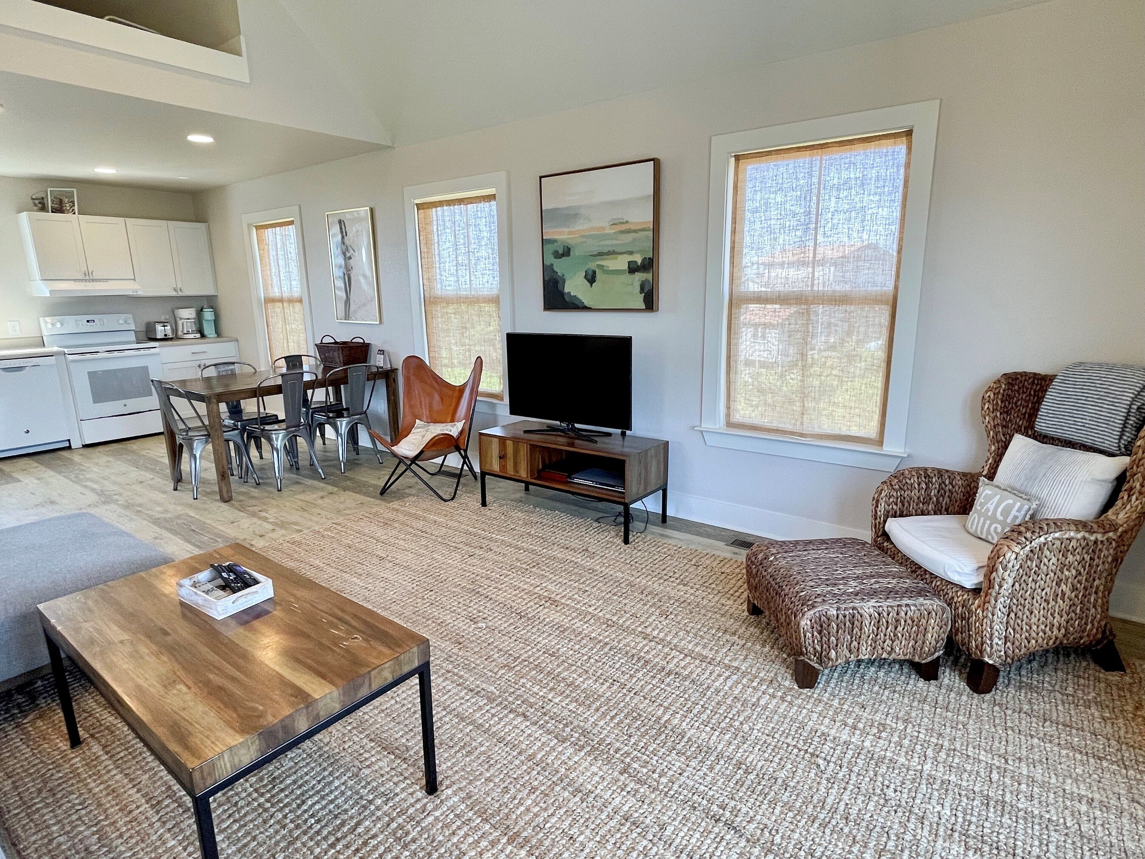 A modern living room with a TV, a dining area, and a kitchen in the background.