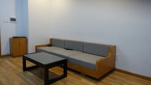 Ein Zimmer mit Holzboden, einem grauen Sofa, einem Glastisch und einem Holzschrank.