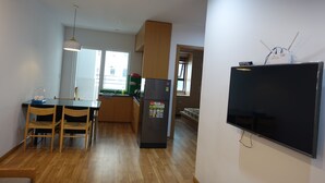 Eine kleine Küche mit Holzausstattung, einem Kühlschrank, einem Esstisch mit Stühlen und einem flachbildfernseher an der Wand.