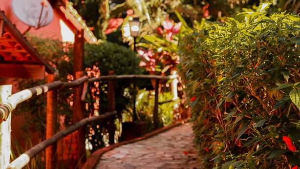 A stone pathway in a garden area with a wooden fence on one side and a variety of plants and flowers. -  Pousada Mirante do Penedo (Itatiaia)