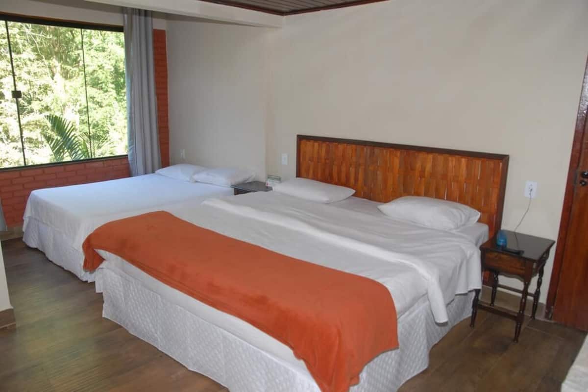 Habitación con dos camas, cabecera de madera, mesita de noche y ventana con vistas a zonas verdes.