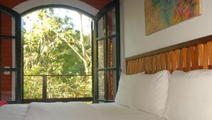 A bed with white linens in a room with a large window and a wooden headboard. -  Pousada Mirante do Penedo (Itatiaia)