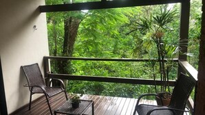 A balcony with two wicker chairs and a small table, overlooking a lush green forest. -  Pousada Mirante do Penedo (Itatiaia)