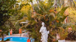 A statue in a lush garden with a pool and a brick structure in the background. -  Pousada Mirante do Penedo (Itatiaia)