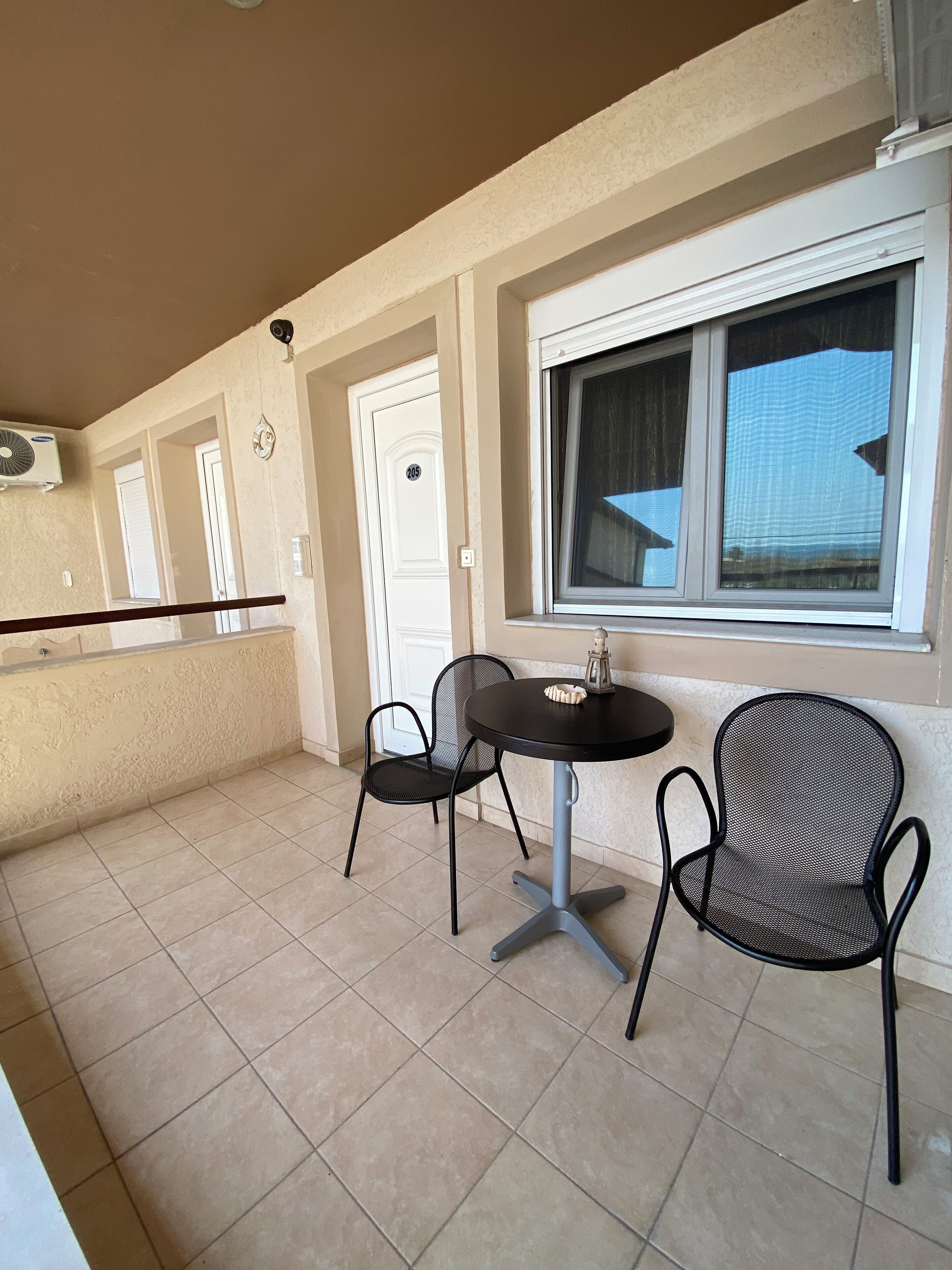 Un balcon avec deux chaises et une table, une porte blanche et une fenêtre donnant sur un beau paysage.