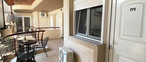 Een balkon met een tafel en stoelen, een witte deur met het nummer 204, en een airconditioning.