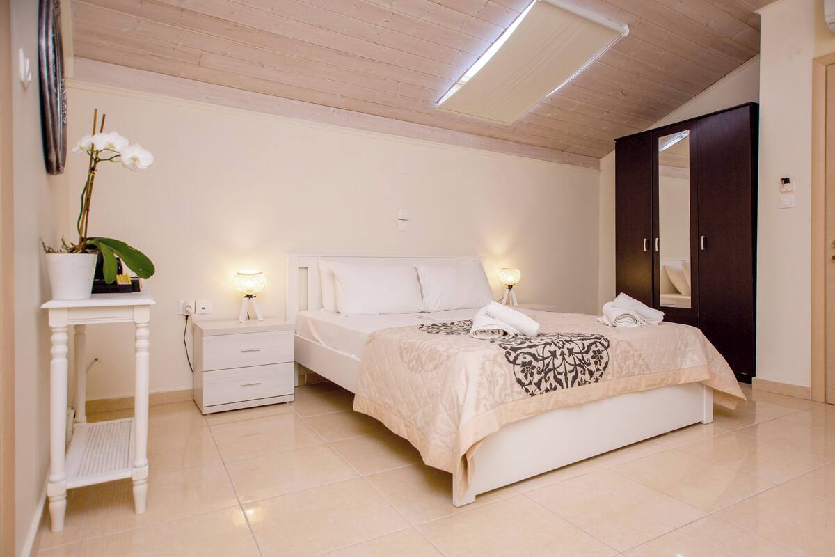 Un dormitorio con cama, mesitas de noche, una planta en maceta y un armario.