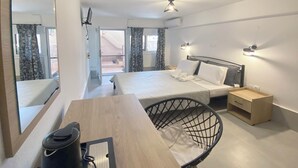 Une chambre d’hôtel comprenant un lit, des tables de chevet, un bureau avec une chaise, un miroir et une vue sur l’extérieur.