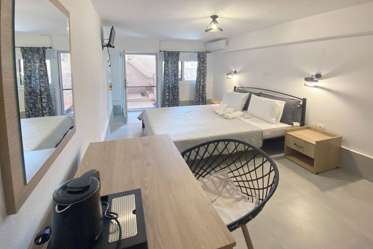 Habitación de hotel con cama, mesitas de noche, un escritorio con silla, un espejo y vistas al exterior.