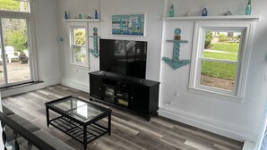 A living room with a TV, black entertainment unit, glass coffee table, and nautical-themed decor.