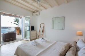 A bedroom with a bed, a chair, a ladder, and a view of the sea. - Villa Isabella (Mykonos)