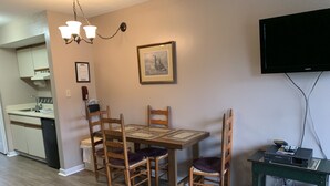 Zona pranzo con tavolo e sedie in legno, un lampadario, un quadro incorniciato e una televisione su un mobile.