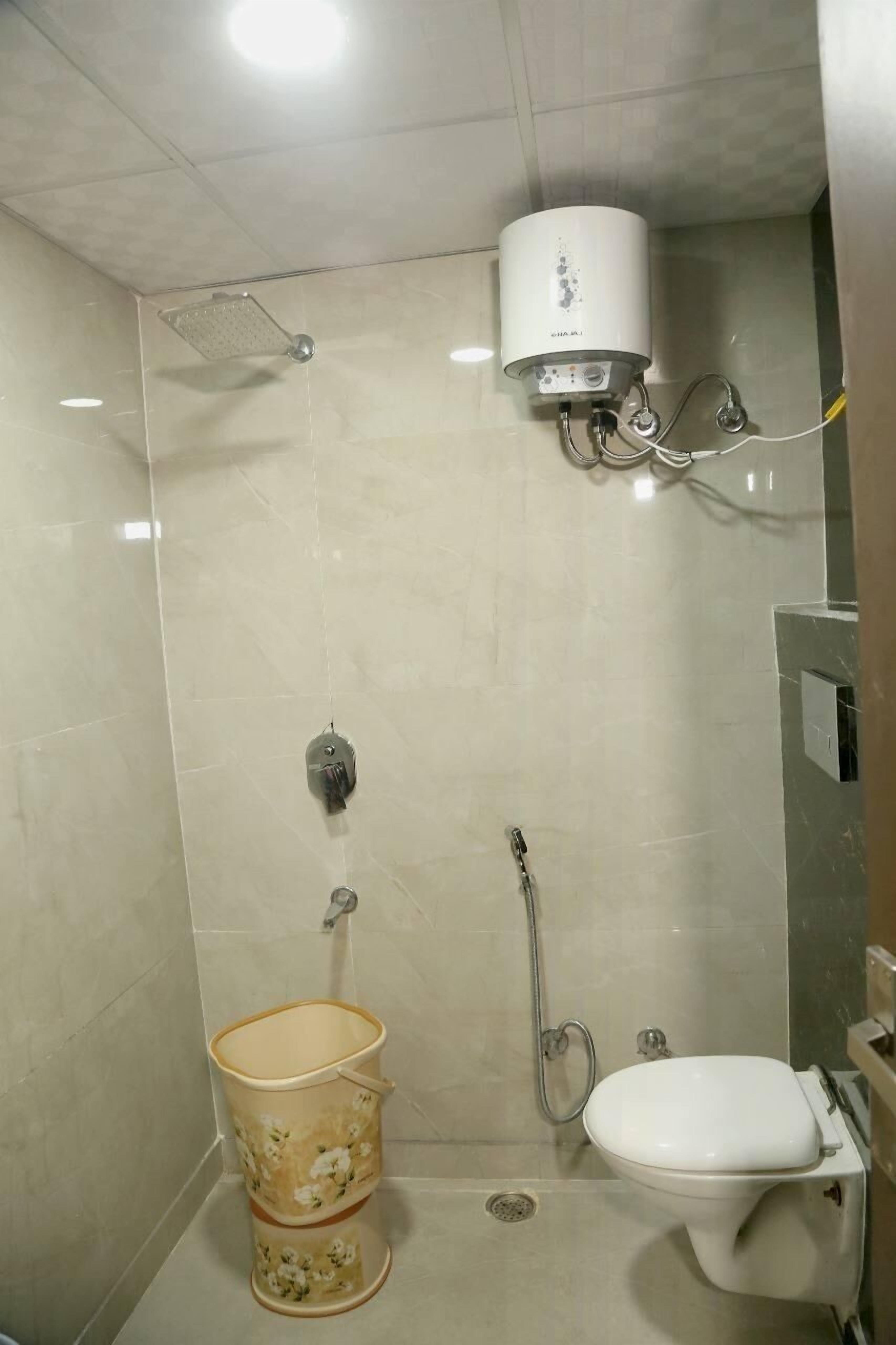 A small, tiled bathroom with a shower, toilet, and a water heater mounted on the wall.