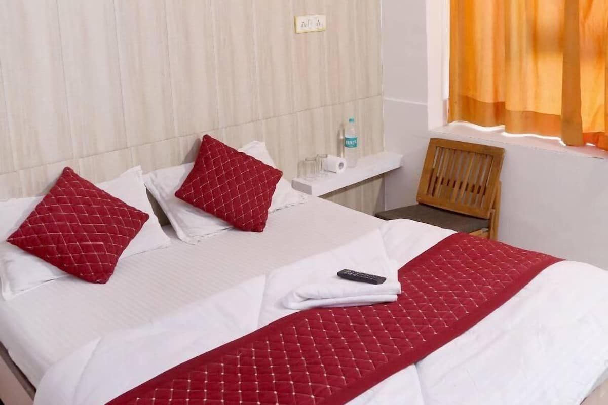 Una habitación de hotel con cama, mesita de noche, aire acondicionado y una ventana con cortinas.