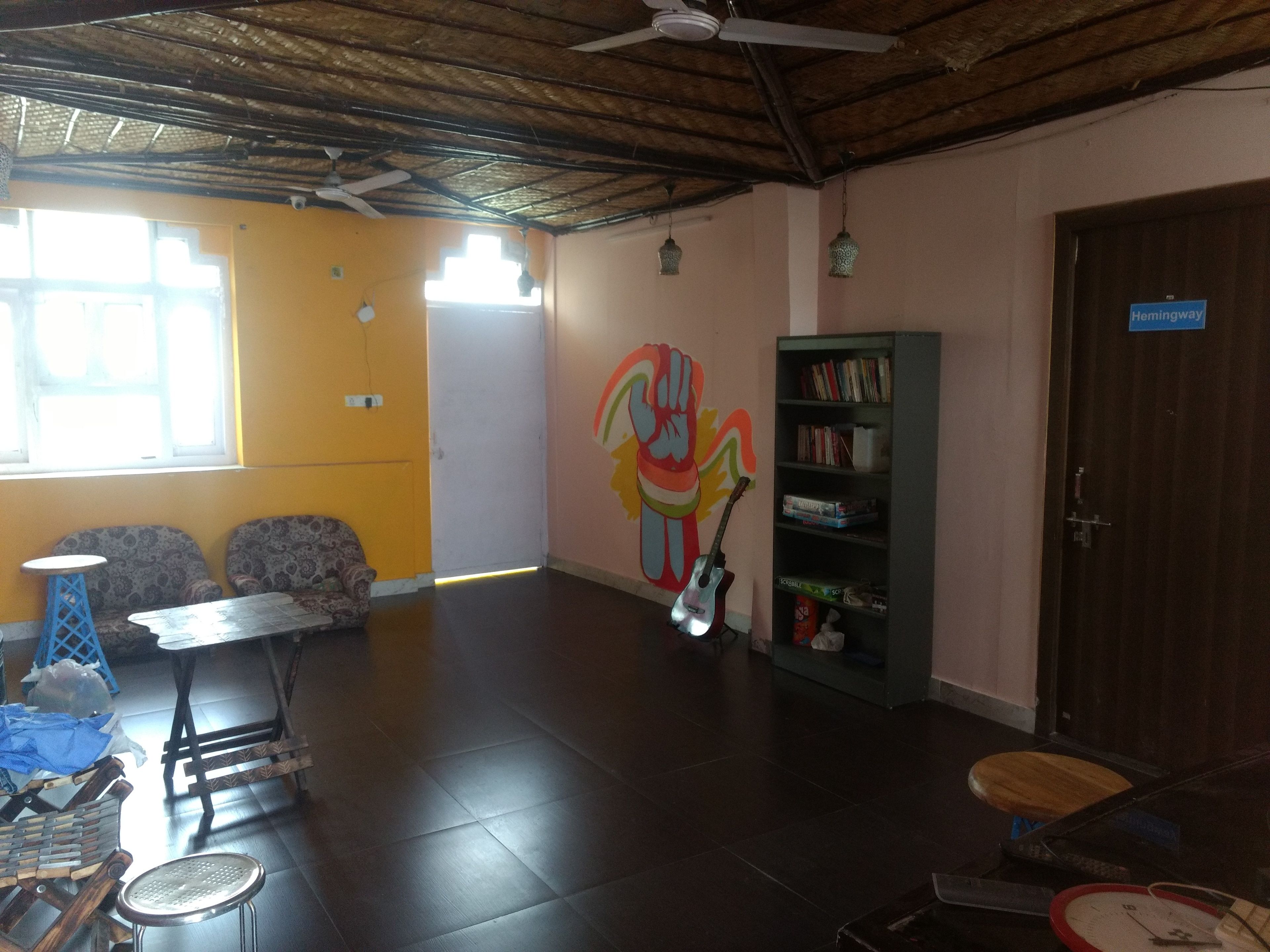 A room with a high ceiling, a bookshelf, a guitar, and a door labeled "Hemingway".