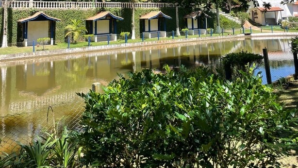 A serene lakeside area with a row of small, traditional-style huts along the water's edge, surrounded by lush greenery and tall trees. - Beautiful site in Mairiporã - SP Wi - Fi (mairiporã)