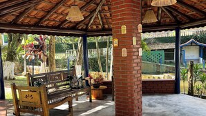 A covered outdoor seating area with wooden benches, a brick pillar, and hanging wicker lamps. - Beautiful site in Mairiporã - SP Wi - Fi (mairiporã)