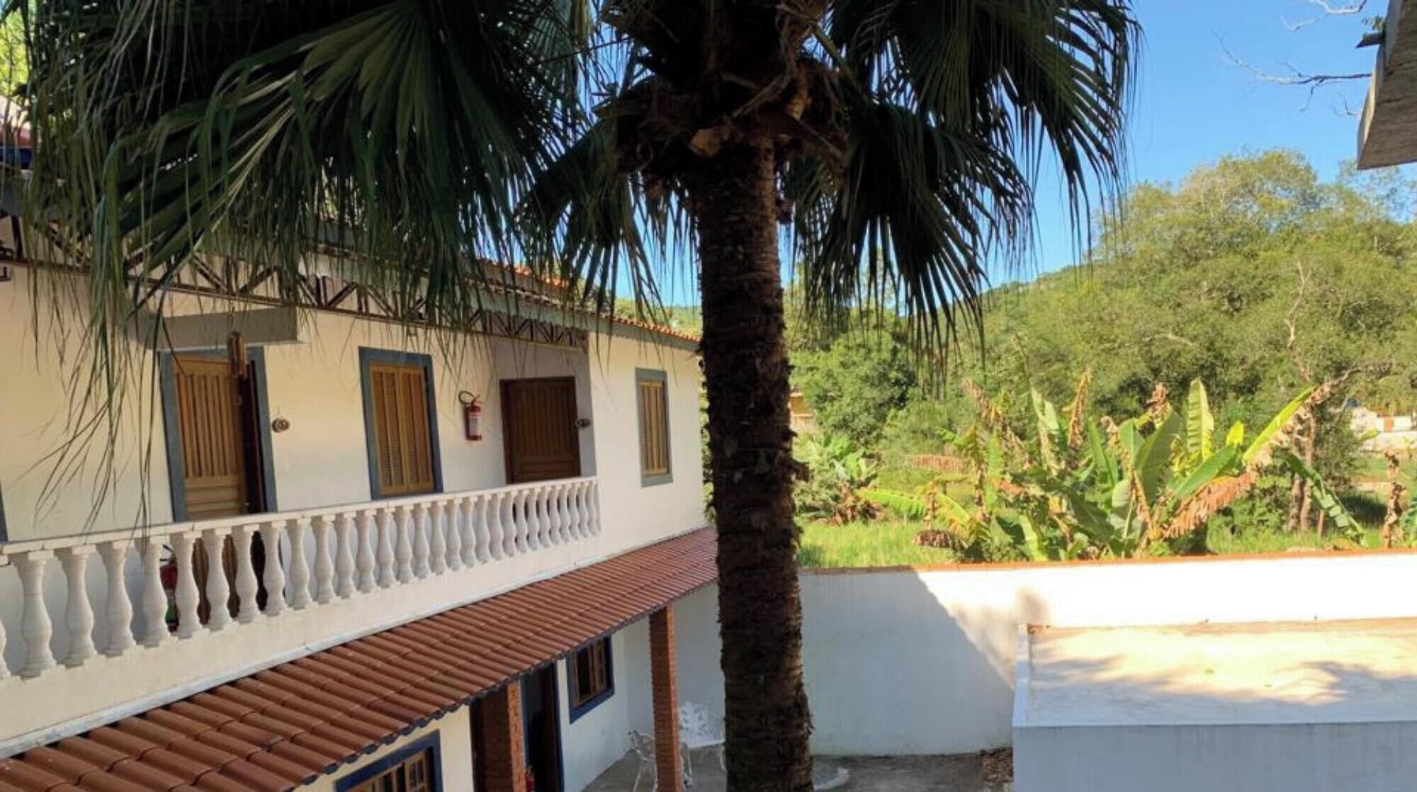 A two-story building with a balcony, a palm tree, and a view of greenery.