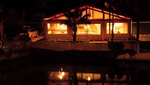A house with a visible kitchen area, a car parked outside, and a pond in the foreground. - Beautiful site in Mairiporã - SP Wi - Fi (mairiporã)