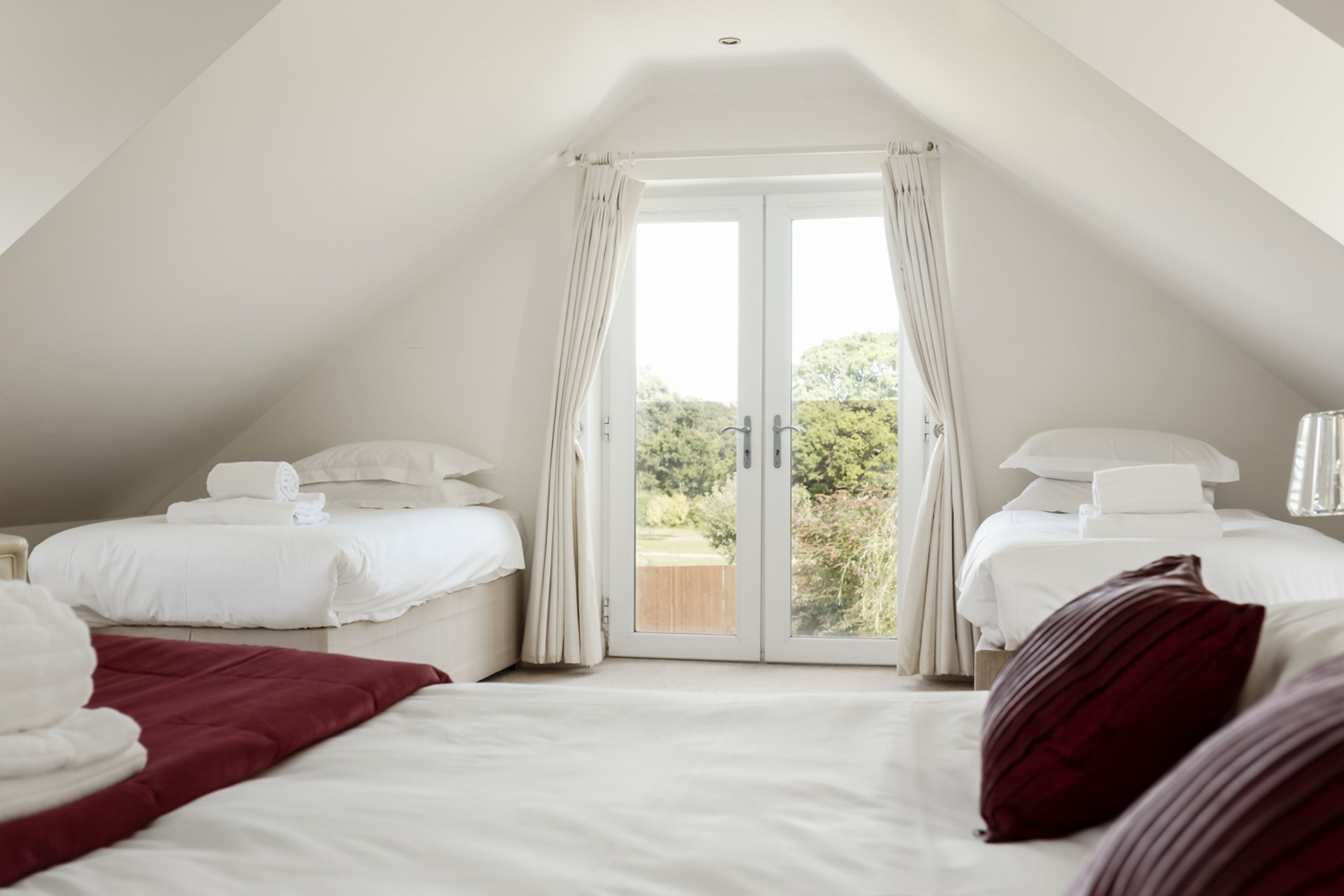 A bedroom with two beds, a large window, and a view of greenery outside.
